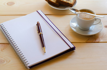 Creative breakfast. Cup of coffee, open note pad with pen and mobile phone on wooden background.  Concept for writing.