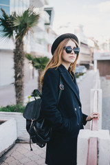 Young beautiful woman wearing hat and coat standing on the embankment near sea