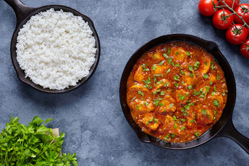 Chicken tikka masala traditional Asian spicy butter meat food with tomatoes, parsley and rice in cast iron skillet