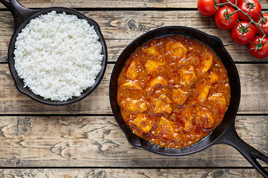 Traditional chicken tikka masala Indian spicy meat food with rice in cast iron skillet on vintage wooden background
