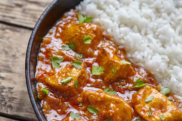 Chicken tikka masala traditional Indian spicy curry national meat food with rice and parsley in cast iron skillet on vintage wooden background. Karahi chicken or korma vindaloo recipe.