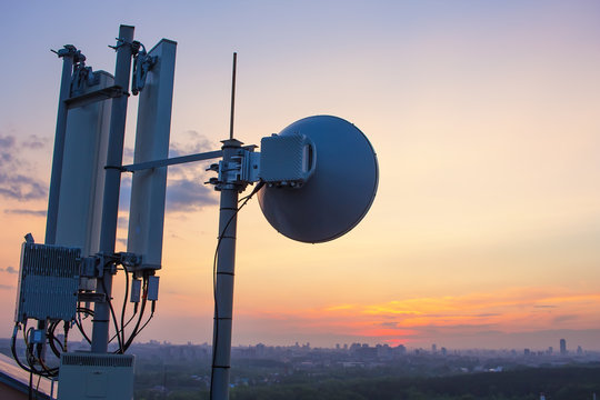 base station with radio relay antenna on the background of a sunset over the city