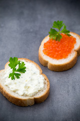 Bread with fresh cream cheese and red caviar on table.