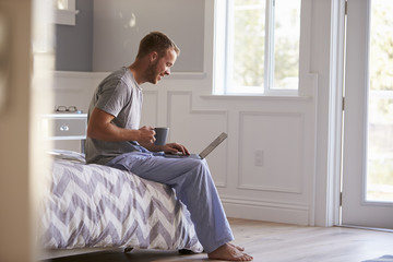 Man Wearing Pajamas Using Laptop Computer In Bedroom