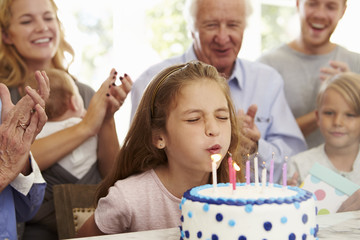 Obraz na płótnie Canvas Girl Blows Out Birthday Cake Candles At Family Party