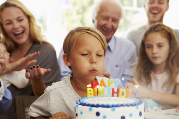 Boy Blows Out Birthday Cake Candles At Family Party