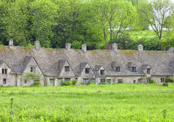 Row of traditional English cottages in charming Cotswolds village Bibury with meadow in front and trees in the back garden