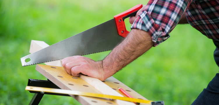 Carpenter sawing a wooden square with a wood saw