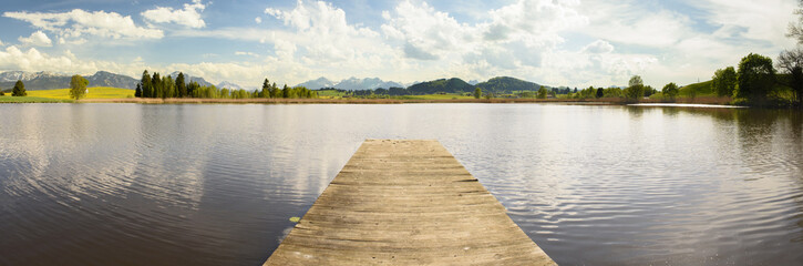 Obraz premium Panorama Landschaft in Bayern im Allgäu bei Fuessen mit Badesteg im See