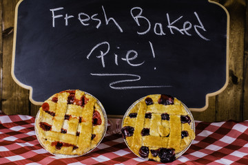 fruit pies on checked table cloth in front of chalkboard advertising fresh baked pie © zenmaster8