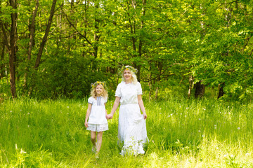 Beautiful family goes hand in hand. Happy family resting on the nature in the summer. Mom and daughter with wreath in the flowers in the park