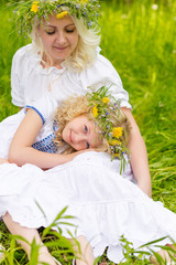 Beautiful and happy mum and daughter with wreaths on the head outdoors in the summer