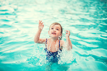 Little happy girl in swimming pool. Kid splashing on pool