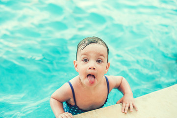 Fototapeta na wymiar Happy child in swimming pool, beautiful girl swims and showing tongue