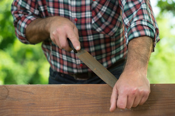 Carpenter using a wood rasp on the edge of a board