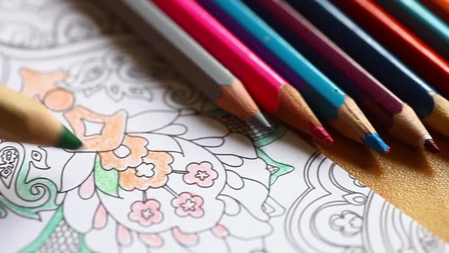 Sliding video of some pencils and a hand coloring an adult coloring book.