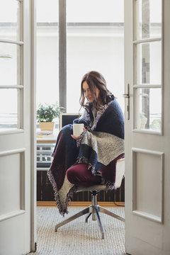 Woman wrapped in blanket drinking coffee