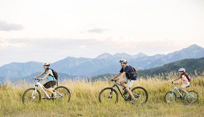 Caucasian family riding mountain bikes in field