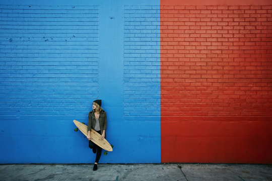 Caucasian woman holding skateboard at painted wall