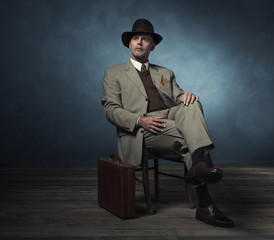 Fashionable retro 1940 business man with hat sitting on chair in