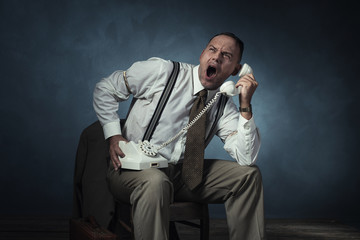 Screaming angry retro 1940 man on the phone sitting on chair in