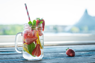 Jug with lemon and strawberry infused water on a rustic wooden surface