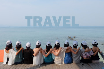 women friend group sit make arm hug hold around their friend's shoulder on wooden pier. They wear same design caps with FRIENDSHIP alphabets on each one. 
looking at TRAVEL word on blue sea sky.
