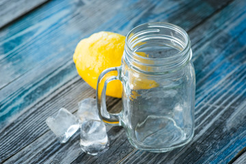 Glass jar and melted ice cubes with lemon on a rustic wooden board