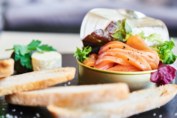Poorly salted salmon served in a tin and crispy baguette on a stone plaque closeup