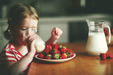 happy child girl drinks milk and eats strawberries in summer hom