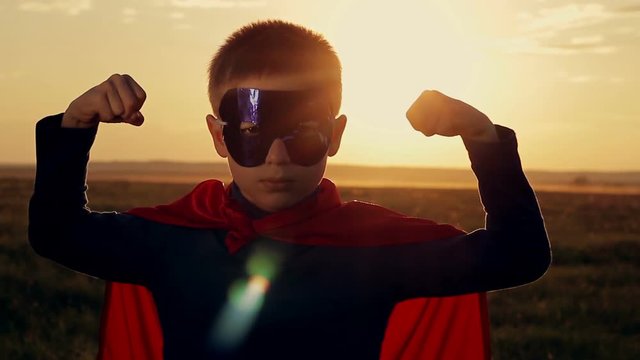 superhero boy running on the green field at sunset