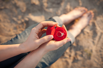 female's hand hold gift box with golden engagement ring;