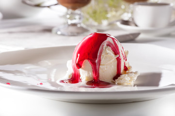 ice cream scoop with berry syrup on white plate close-up against decorated table
