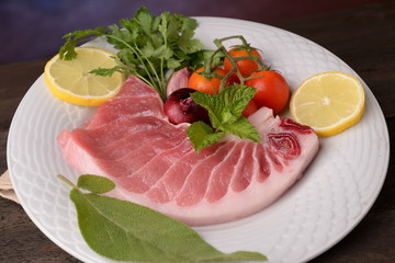 tuna steak raw on white plate with herbs and lemon