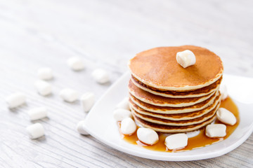 Tasty pancake on a white plate, wooden background, maple syrup