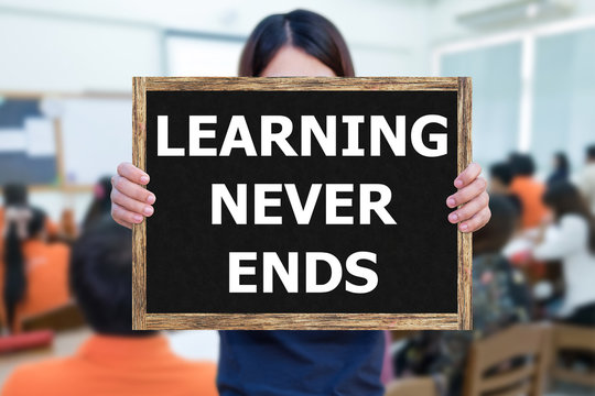 LEARNING NEVER ENDS message on the blackboard wooden frame on hand woman with blurred student study learning in classroom.