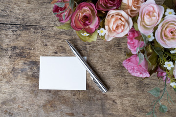 Vintage Empty white note card and pen with rose flowers on rusty wooden background . 