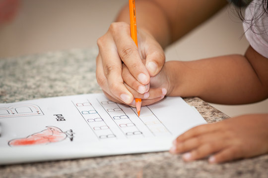 Mother's hand holding child hand writing her homework 