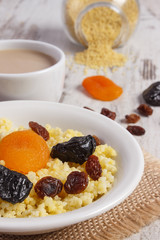 Cooked millet groats on white plate and cup of coffee with milk, healthy food and nutrition