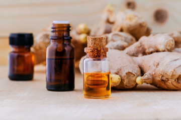 Bottles of ginger oil and ginger on wooden background with selec