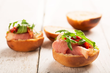 Sandwich with duck breast and arugula on a white wooden table