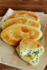 Fried pies with cottage cheese filling. Patties with cottage cheese, green onion and dill. Cheap recipe for homemade fried pies on a wooden background in rustic style. Easy meal idea. Close-up