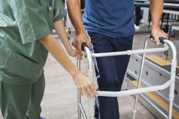 Midsection Of Nurse Assisting Senior Man To Walk Using Walker