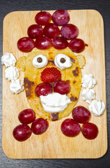 Funny looking face made of sliced grapes, strawberries and pancake, as seen from above