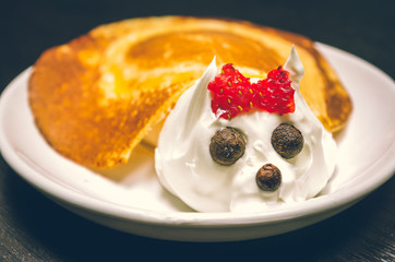 Funny looking turtle portrait made from pancake and cream with chocolate eyes, lying on white plate 
