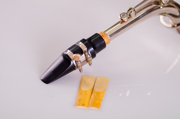 Closeup dismantled mouth piece from saxophone and two reeds lying on white surface