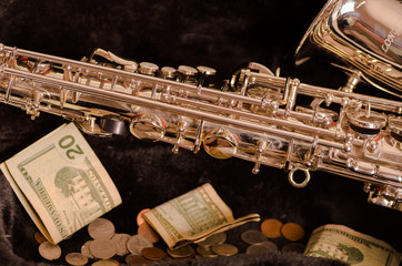 Obraz premium Shiny saxophone lying across open instrumental casing with black velvet interior and pile of money inside