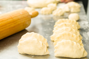 Closeup small delicious empanadas lined up before baking, rolling pin background