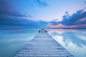 Fototapeta na wymiar Holzsteg mit Bank am See zum Sonnenuntergang