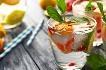 Refreshing cocktail with ice, mint, pomegranate seeds and slices of fruits on wooden background